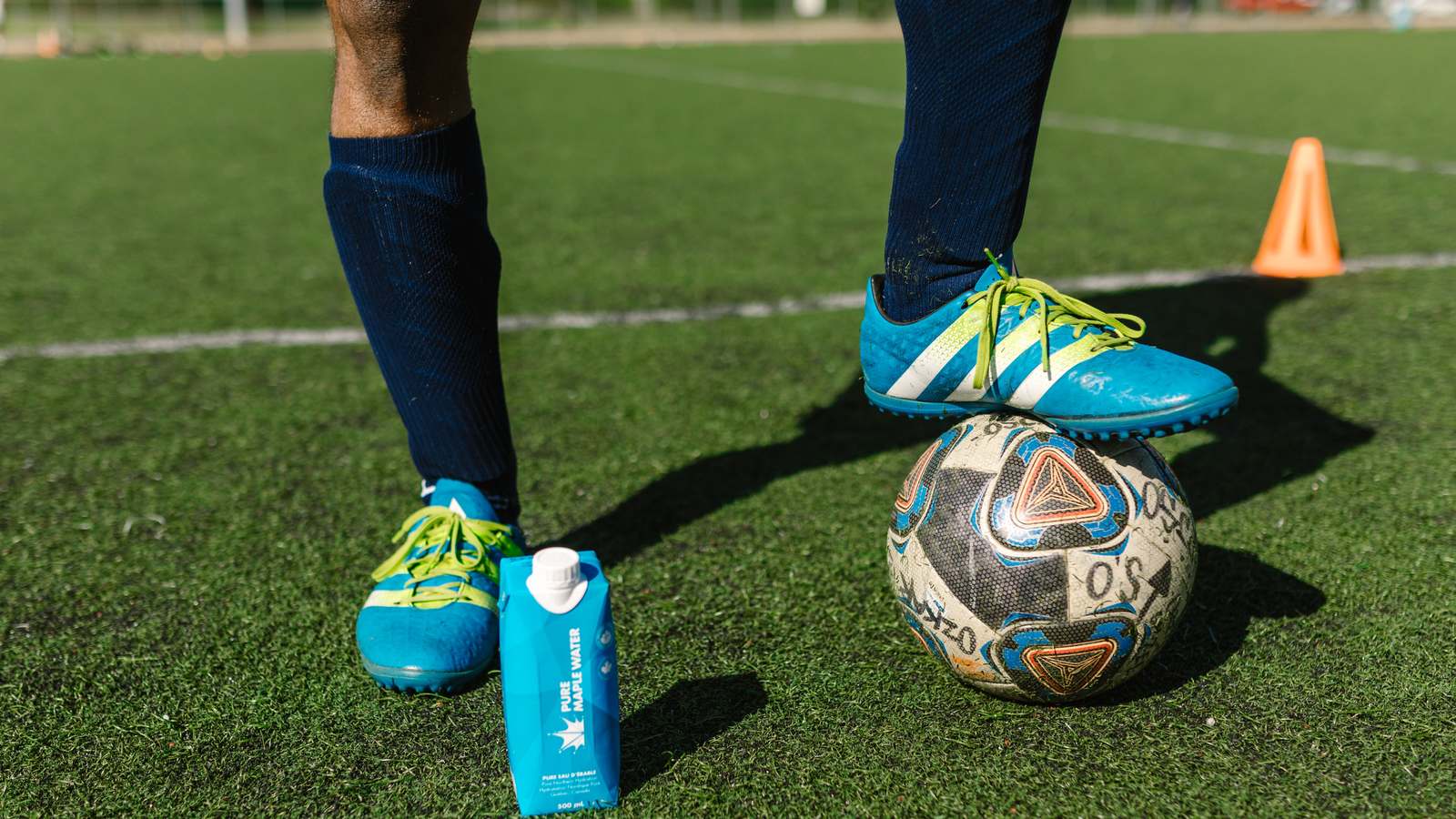 Chaussures de football bleues à côté d'un ballon sur terrain synthétique