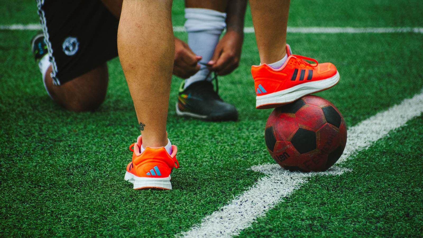 Chaussures de football orange devant un ballon, joueur en train de se chausser